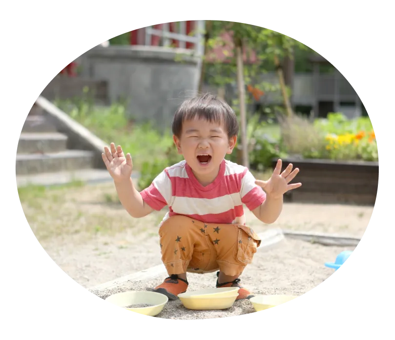両手を広げて座り込み、笑顔でこちらを見る子どもの写真
